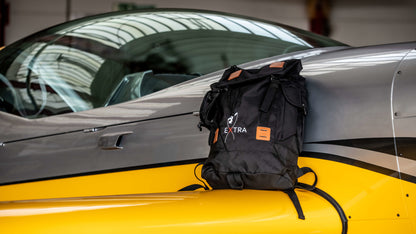 Produktbild des Extra Reiserucksacks, abgelegt auf dem rechten Flügel einer silber-gelben Extra NG. 